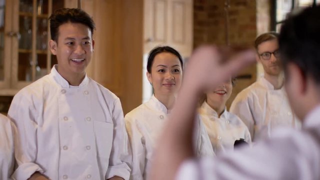  Professional chef talking to happy young trainees in cookery school