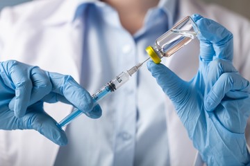 Hand holding syringe and vaccine.