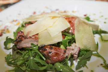 A dish of pork with arugula and parmesan cheese