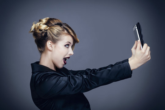 Portrait d'une jeune femme , de profil, se prenant en photo avec sa tablette tactile