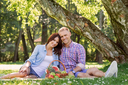 Beautiful couple having a lovely picnic in the summer park eating fruits.