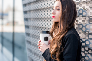 Young caucasian business woman standing with coffee to go outdoors near the modern facade