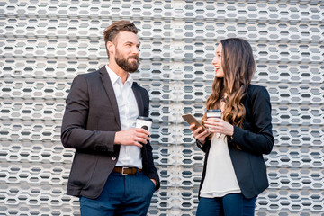 Caucasian business couple talking together standing outdoors during the coffee break near the modern building facade