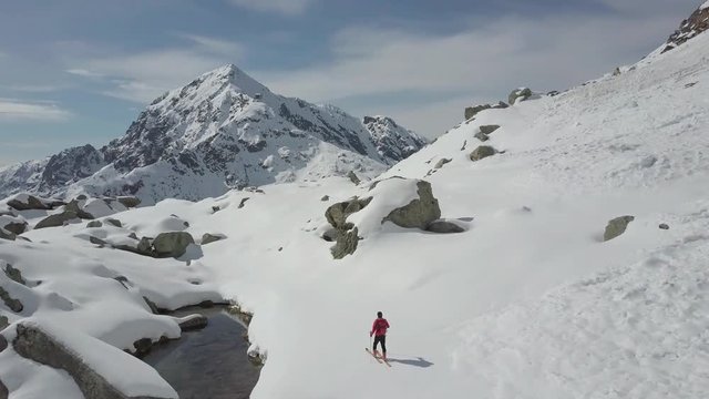 Ski mountaineer walks in a snowy mountain landscape. European Alps, Italy. 4K UHD aerial shot. Log footage version.
