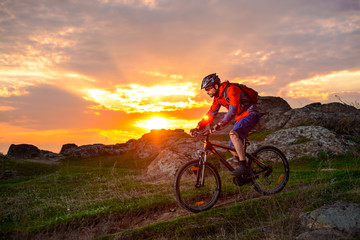 Naklejka na ściany i meble Cyclist Riding Mountain Bike on the Spring Rocky Trail at Beautiful Sunset. Extreme Sports and Adventure Concept.