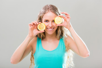 Beautiful young woman showing slices of lemon on gray background.