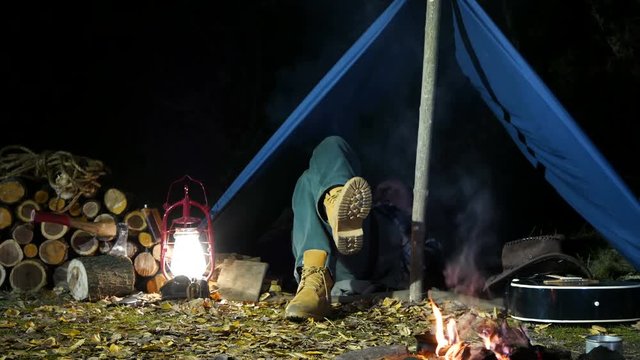Man sleeping under old tent outdoors, near the bonfire.