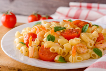 Pasta with shrimps, cherry tomatoes and basil in white plate.