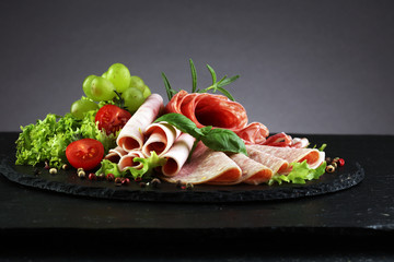 Food tray with delicious salami, pieces of sliced ham, sausage, tomatoes, salad and vegetable - Meat platter with selection