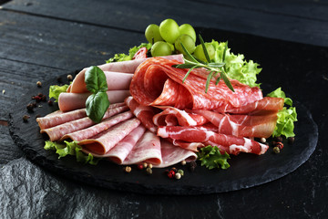 Food tray with delicious salami, pieces of sliced ham, sausage, tomatoes, salad and vegetable - Meat platter with selection