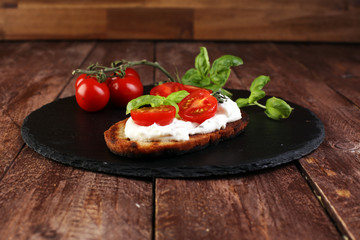 Bread with cream cheese and tomato for lunch table. Sharing antipasti on party or summer picnic time over wooden rustic background.