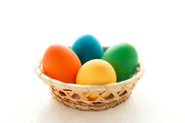 Obraz na płótnie Canvas Multicolored easter eggs in a basket, on a white wooden background. The concept of a holiday and a happy Easter. With space for text