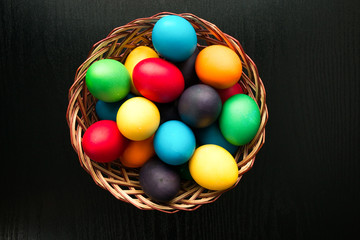 Multicolored easter eggs in a basket on a black wooden background. The concept of a holiday and a happy Easter. And place for text