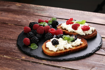 Bread with cheese cream and blackberries and raspberries for lunch table. Sharing antipasti on party or summer picnic time over wooden rustic background.