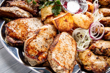 Meat plate with delicious pieces of meat, potatoes, onion and candle on white wooden table