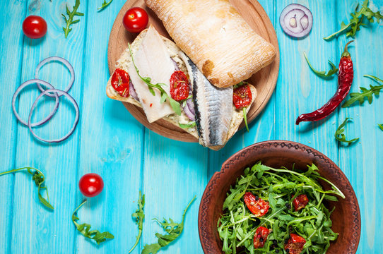 sandwiches with herring and salad with arugula on blue wooden table
