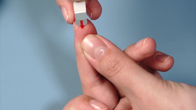 Close up blood sampling for glucometer on test strip. Female hand with drop of blood and test stripe for diabetes testing