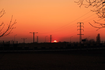 Fototapeta na wymiar Kolorowy, czerwono żółty zachód słońca, maszty elektryczne. 