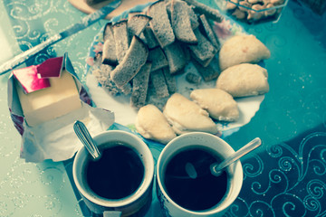 Cups of coffee, homemade curd cakes, crackers and butter with a knife on a glass table