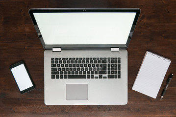 Top view of laptop on desk with smartphone and notepad, dark brown wooden workspace concept