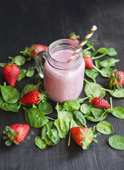 Strawberry green smoothie in a glass jar on a dark wooden table