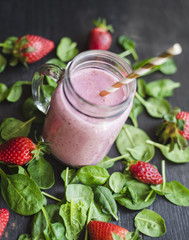 Strawberry green smoothie in a glass jar on a dark wooden table