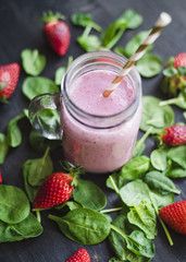 Strawberry green smoothie in a glass jar on a dark wooden table