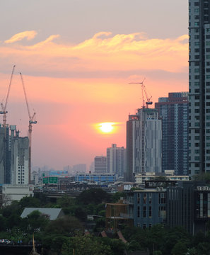 The Sun setting on pastel color sky amongst working cranes of the construction site, vertical image 