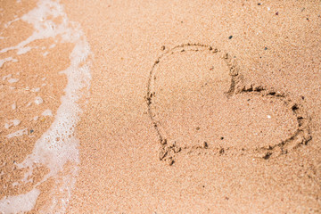 Drawing of a heart on a yellow sand at a beautiful seascape background.