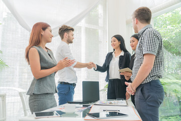 Business people shaking hands to job success while their colleagues applauding and smiling