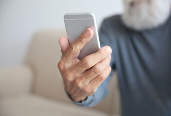 Senior man sitting on sofa with smart phone in room