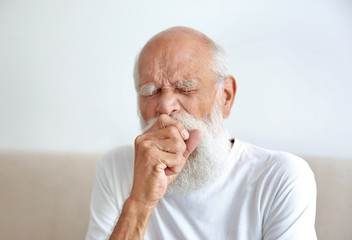 Coughing senior man sitting on sofa