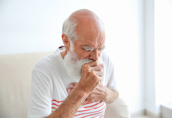 Coughing senior man sitting on sofa - Powered by Adobe
