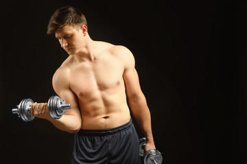 Young handsome sportsman with dumbbells on dark background