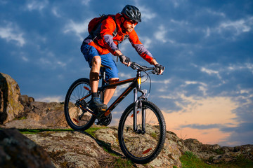 Cyclist Riding Mountain Bike Down Spring Rocky Hill at Beautiful Sunset. Extreme Sports and Adventure Concept.