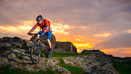 Naklejka na ściany i meble Cyclist Riding Mountain Bike Down Spring Rocky Hill at Beautiful Sunset. Extreme Sports and Adventure Concept.