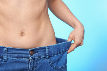 Diet concept. Young beautiful woman in big jeans on light background