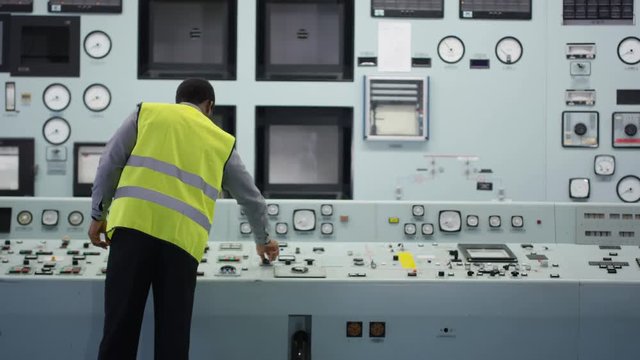 Workers in power plant control room looking at control panel & checking system