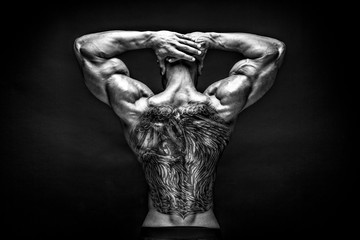 unrecognizable tattoed bodybuilder with outstretched arms on black background. Isolated.