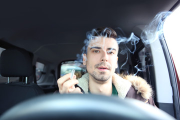 Young man driving a car and smoking cigarette