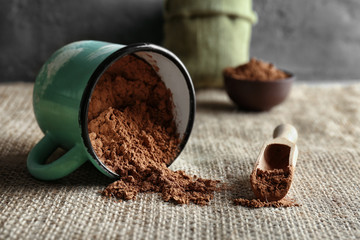 Wooden scoop and metal mug with cocoa powder on kitchen table