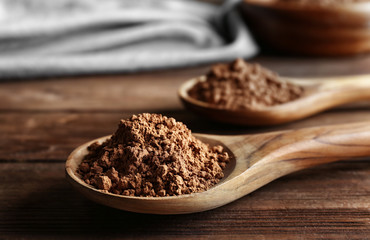 Two spoons with cocoa powder on wooden background