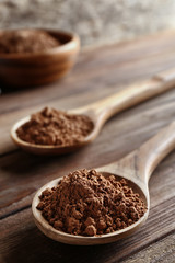 Two spoons with cocoa powder on wooden table