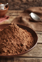 Brown plate with cocoa powder on wooden background