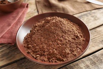 Brown plate with cocoa powder on wooden background