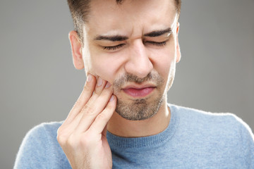 Handsome man suffering from toothache on grey background, closeup