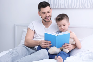 Fototapeta premium Dad and son reading interesting book while sitting on bed at home