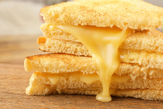 Fototapeta Grilled bread and melting cheese on wooden surface, closeup