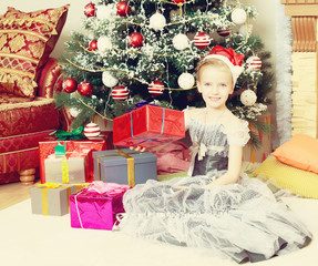 Fototapeta na wymiar Little girl sitting near Christmas tree with a big gift.