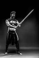 Fototapeta premium Portrait of handsome muscular gladiator with sword. Studio shot. Black background.